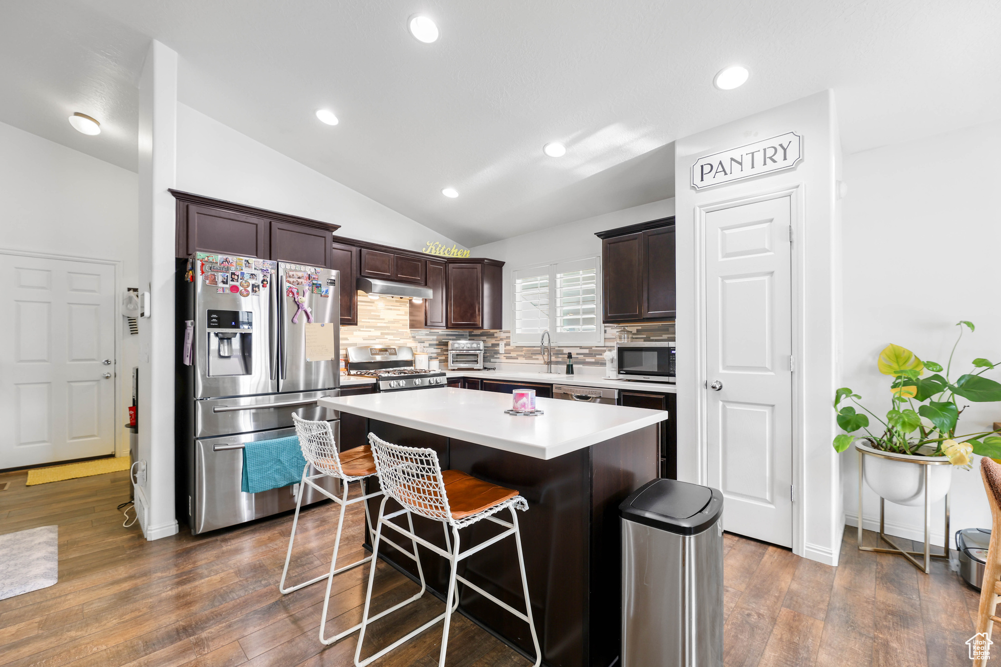 Kitchen with vaulted ceiling, backsplash, a center island, stainless steel appliances, and dark brown cabinets