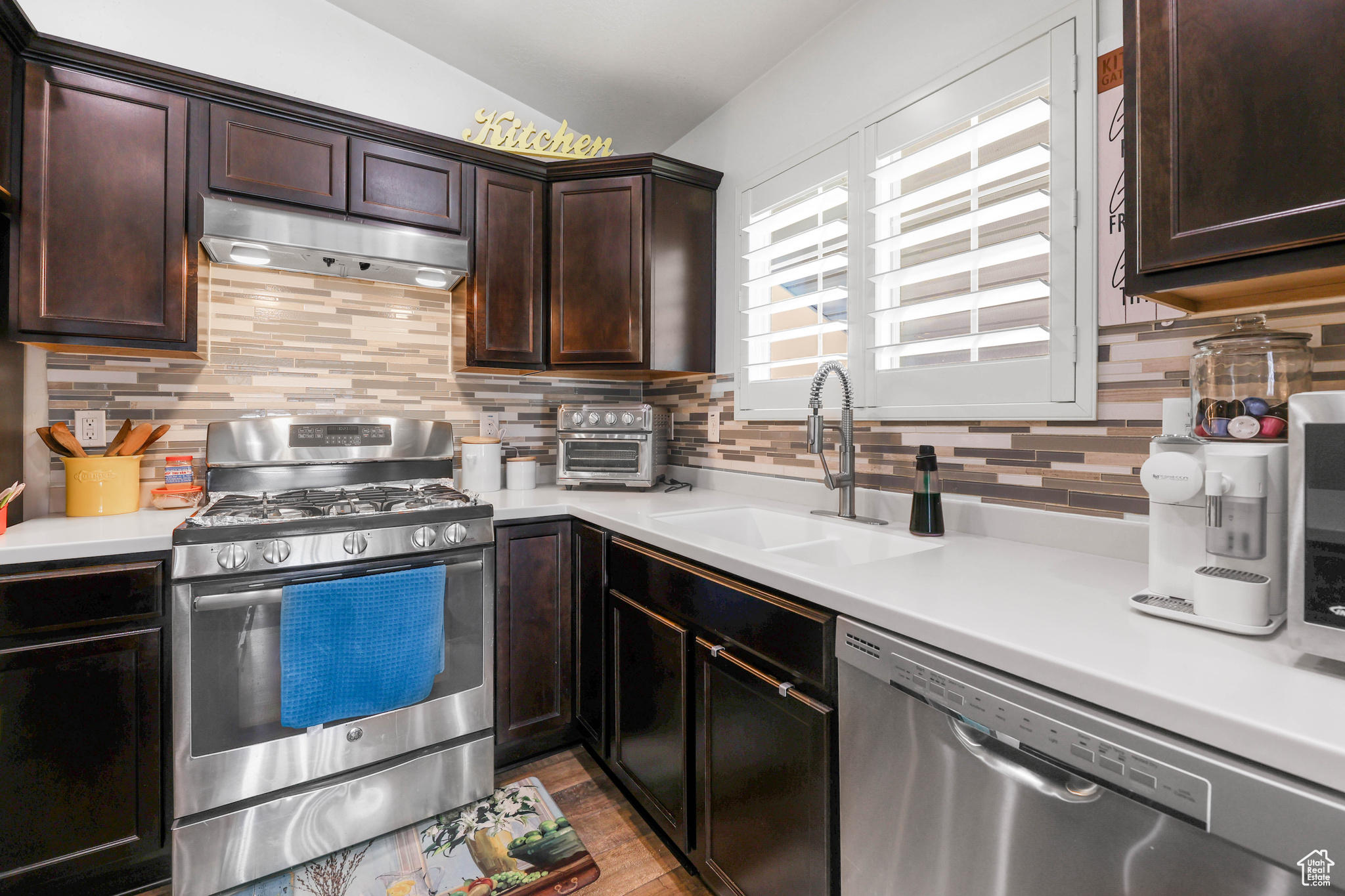 Kitchen featuring sink, backsplash, stainless steel appliances, dark brown cabinetry, and light wood-type flooring