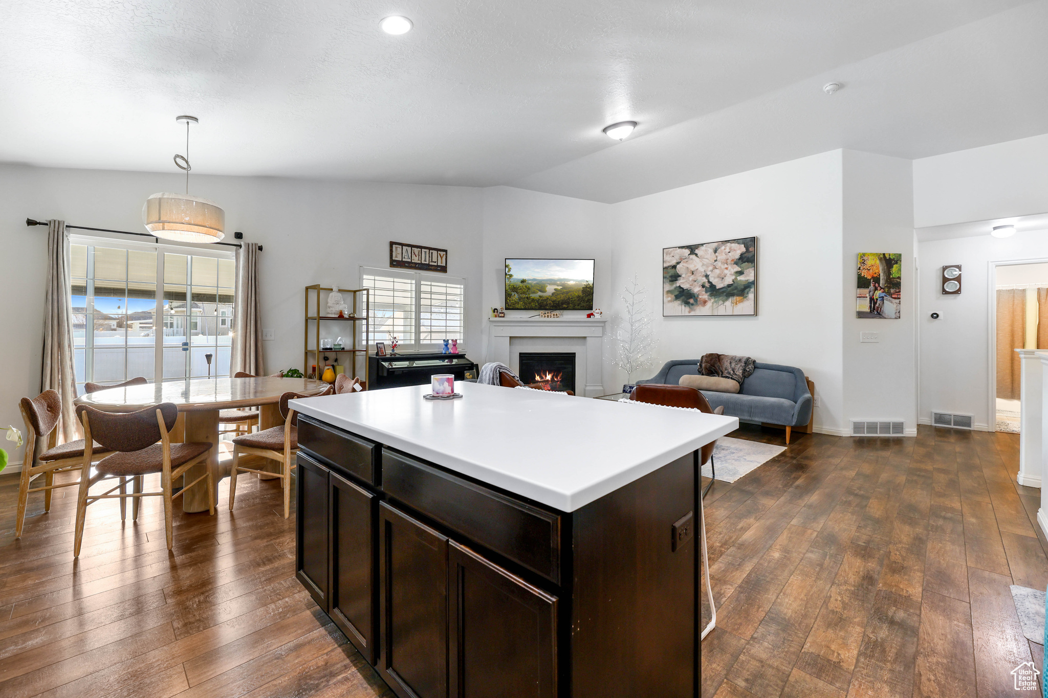 Kitchen with hanging light fixtures, dark brown cabinets, dark wood-type flooring, and a kitchen island