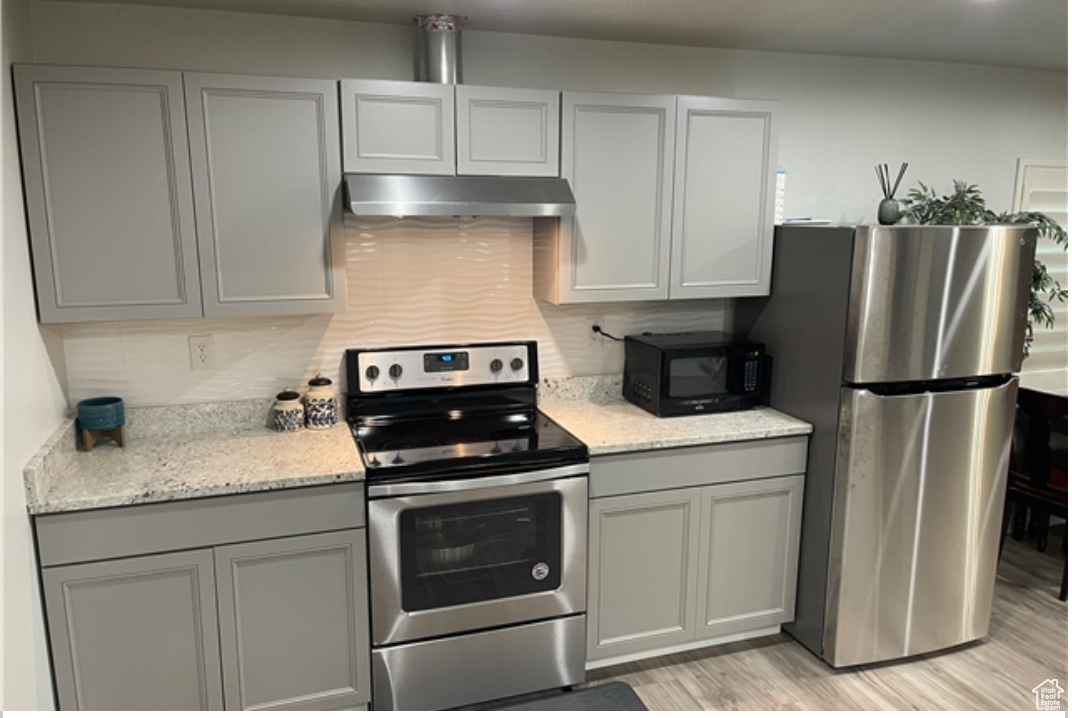 Kitchen featuring appliances with stainless steel finishes, gray cabinetry, backsplash, light stone counters, and light hardwood / wood-style floors