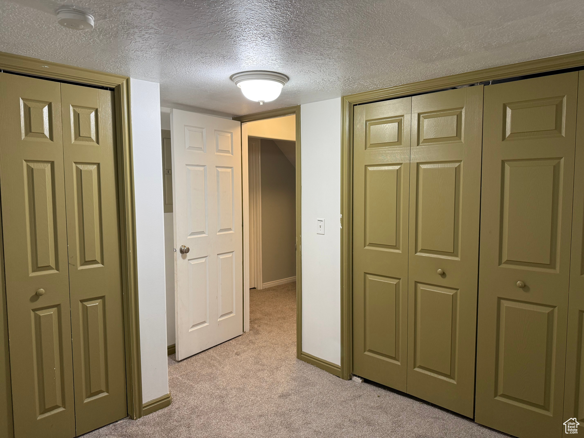 Corridor featuring light carpet and a textured ceiling