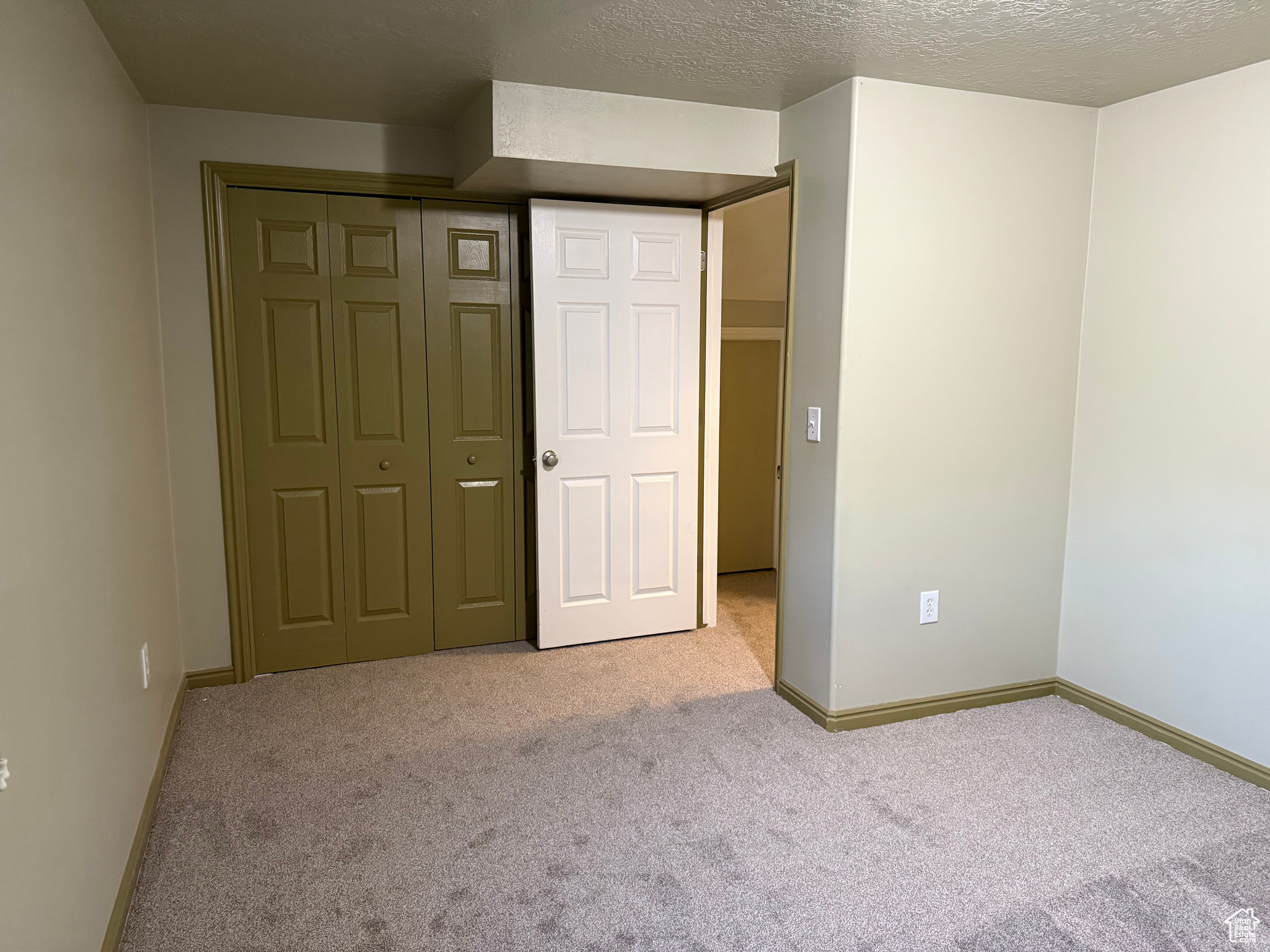 Unfurnished bedroom with light carpet, a closet, and a textured ceiling