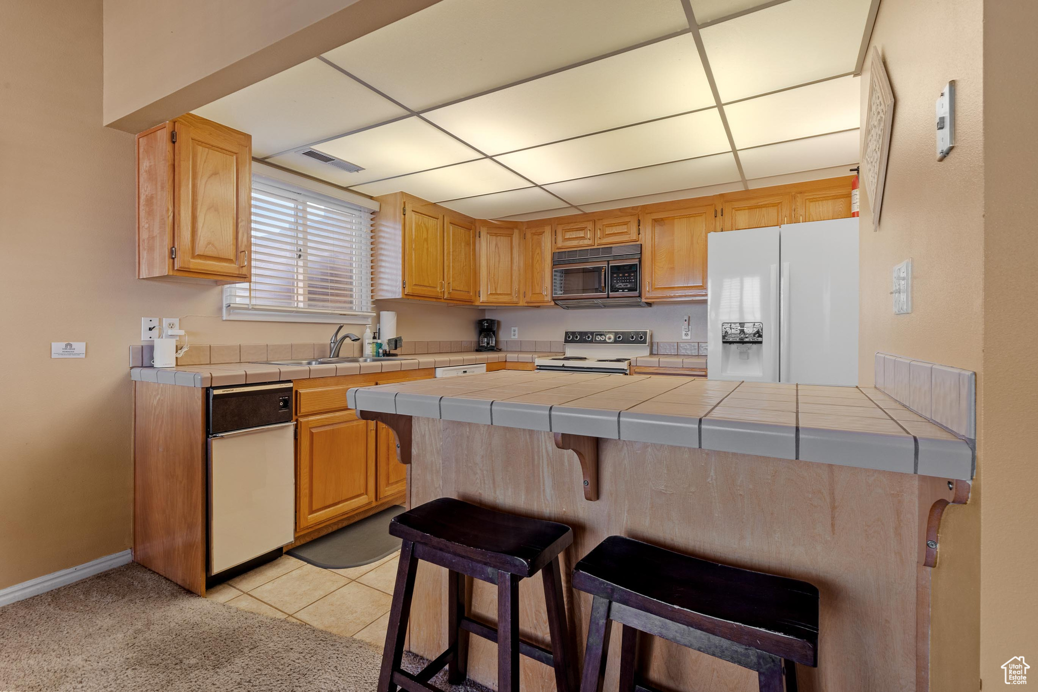 Kitchen featuring light tile patterned flooring, a breakfast bar, sink, tile counters, and white appliances