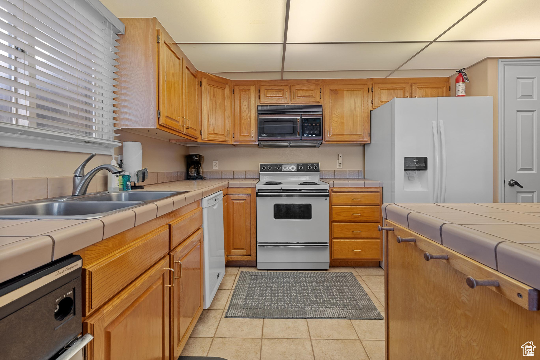 Kitchen with light tile patterned flooring, white appliances, tile counters, and sink