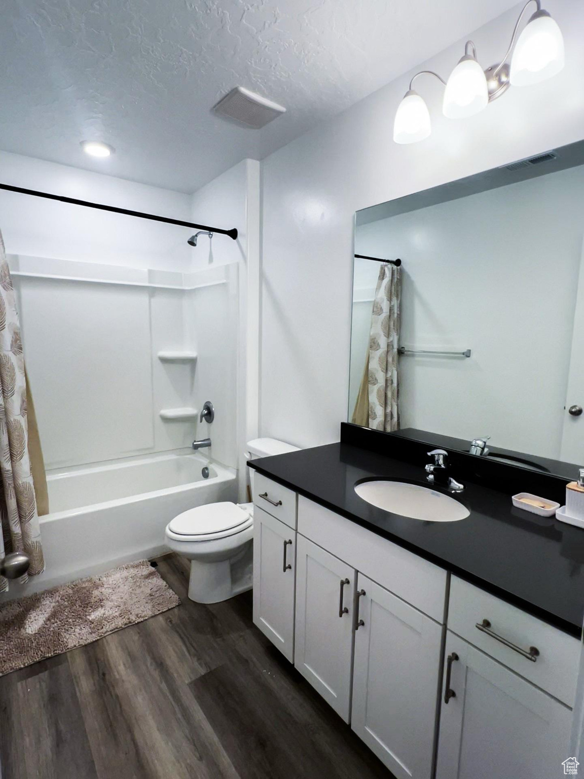 Full bathroom with toilet, wood-type flooring, a textured ceiling, vanity, and shower / bathtub combination with curtain