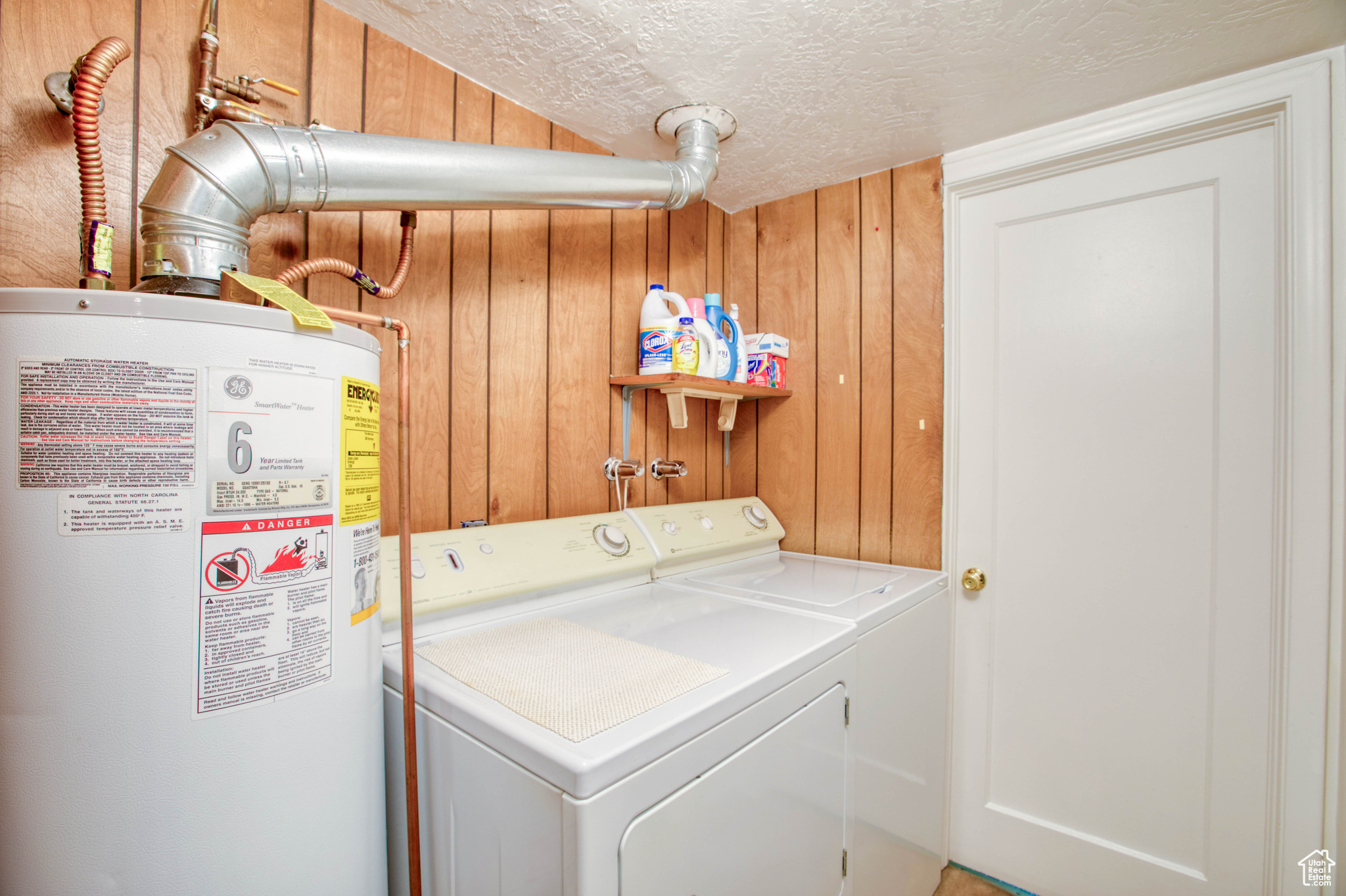 Clothes washing area featuring water heater, washer and dryer, wooden walls, and a textured ceiling