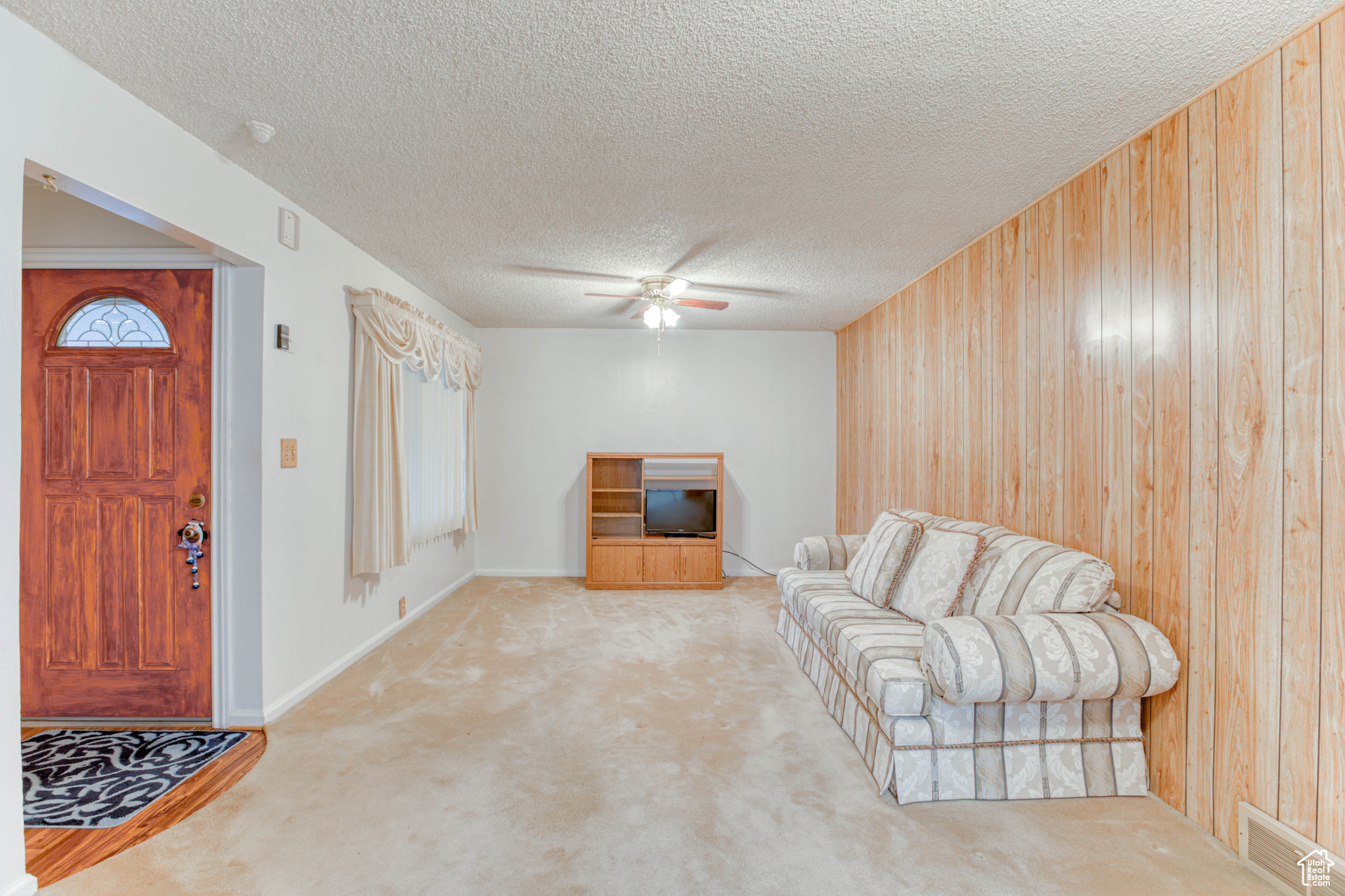 Living room with light colored carpet, a textured ceiling, ceiling fan, and wood walls