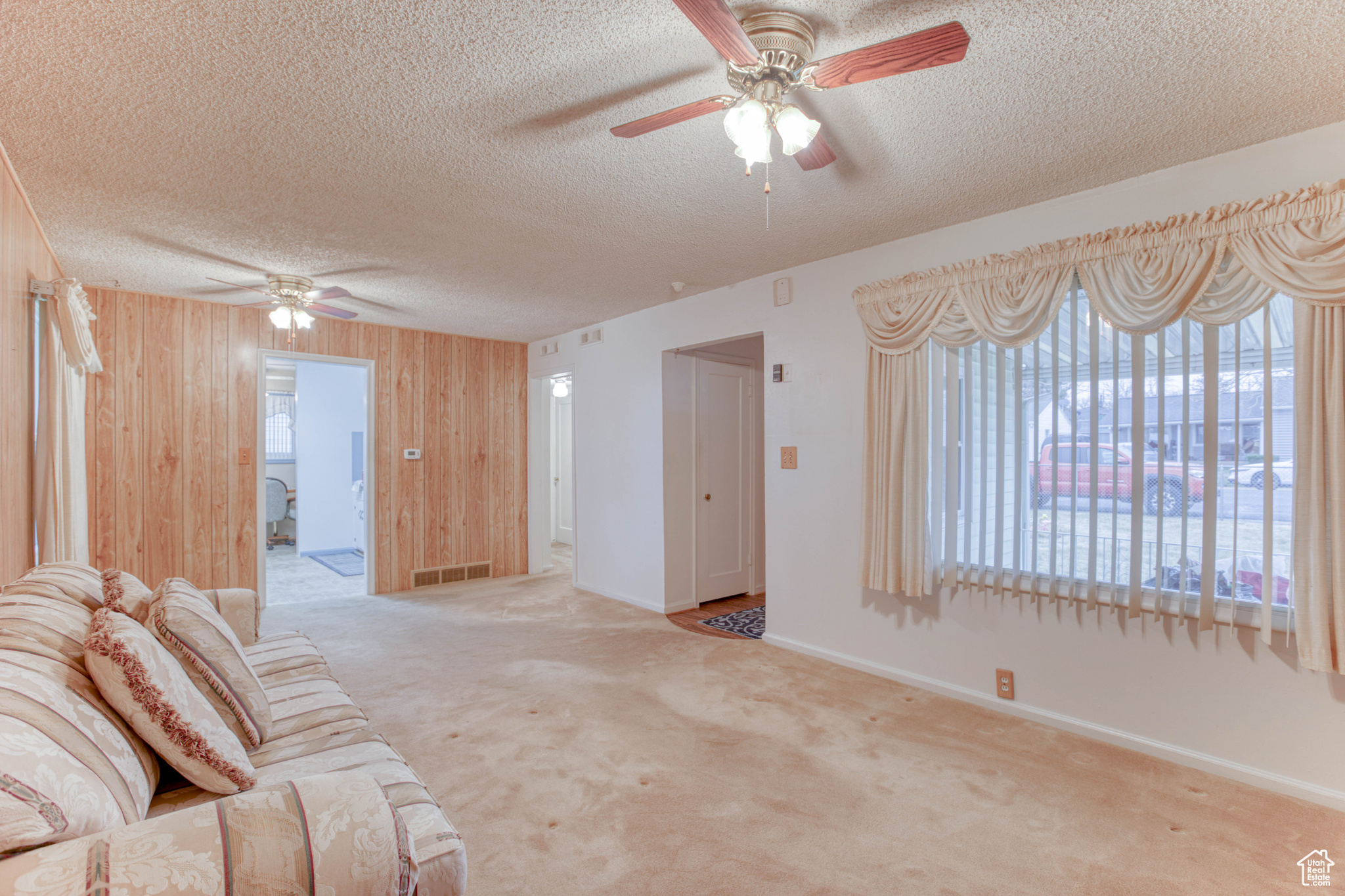 Living room featuring ceiling fan, light carpet, a textured ceiling, and wooden walls