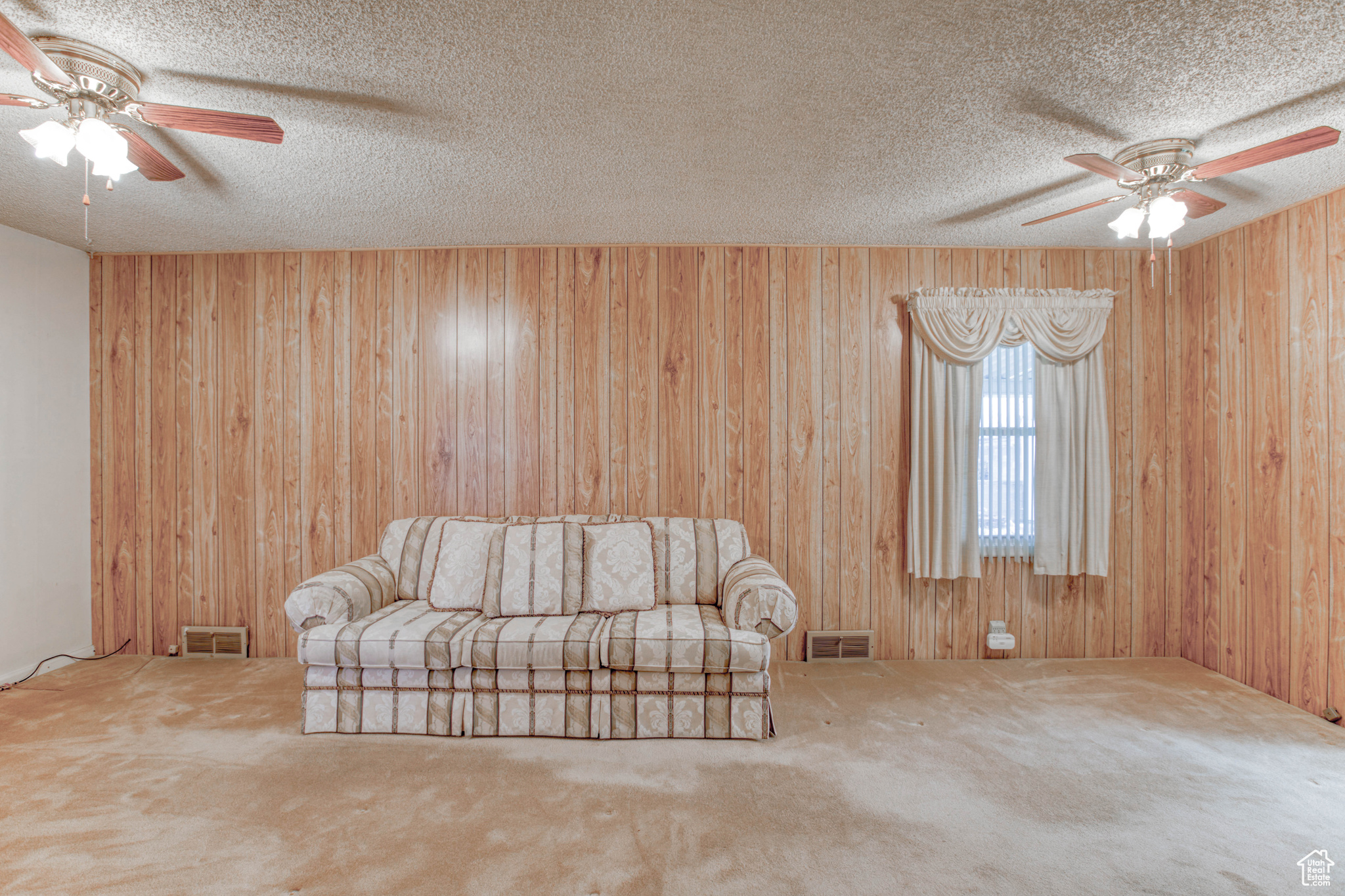 Unfurnished room with carpet floors, ceiling fan, wooden walls, and a textured ceiling