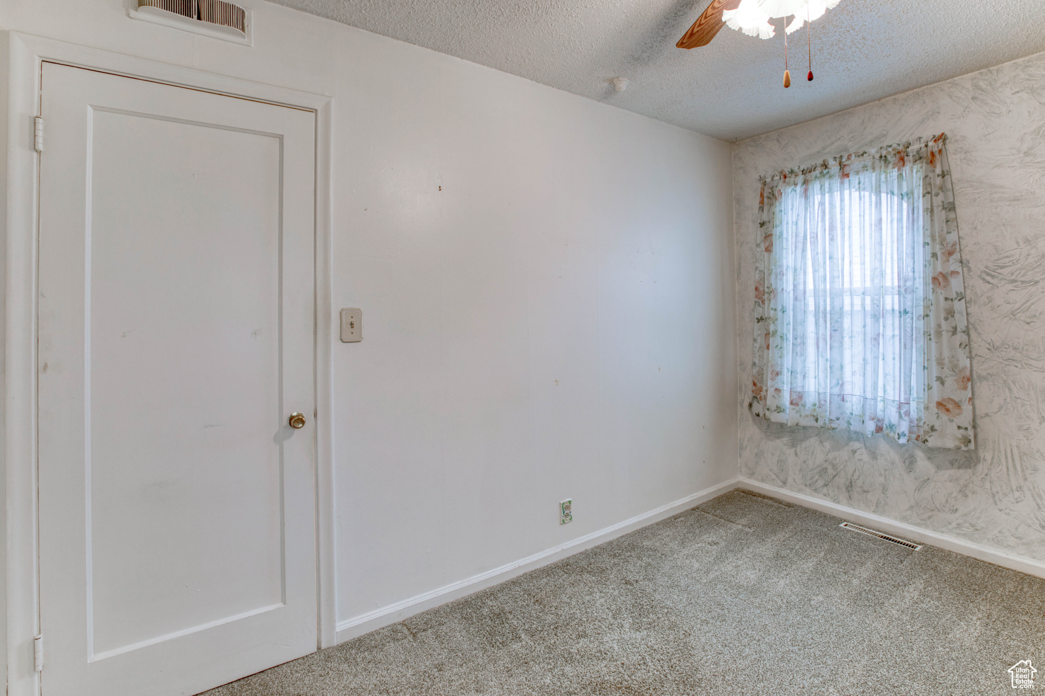 Empty room with ceiling fan, a textured ceiling, and carpet flooring