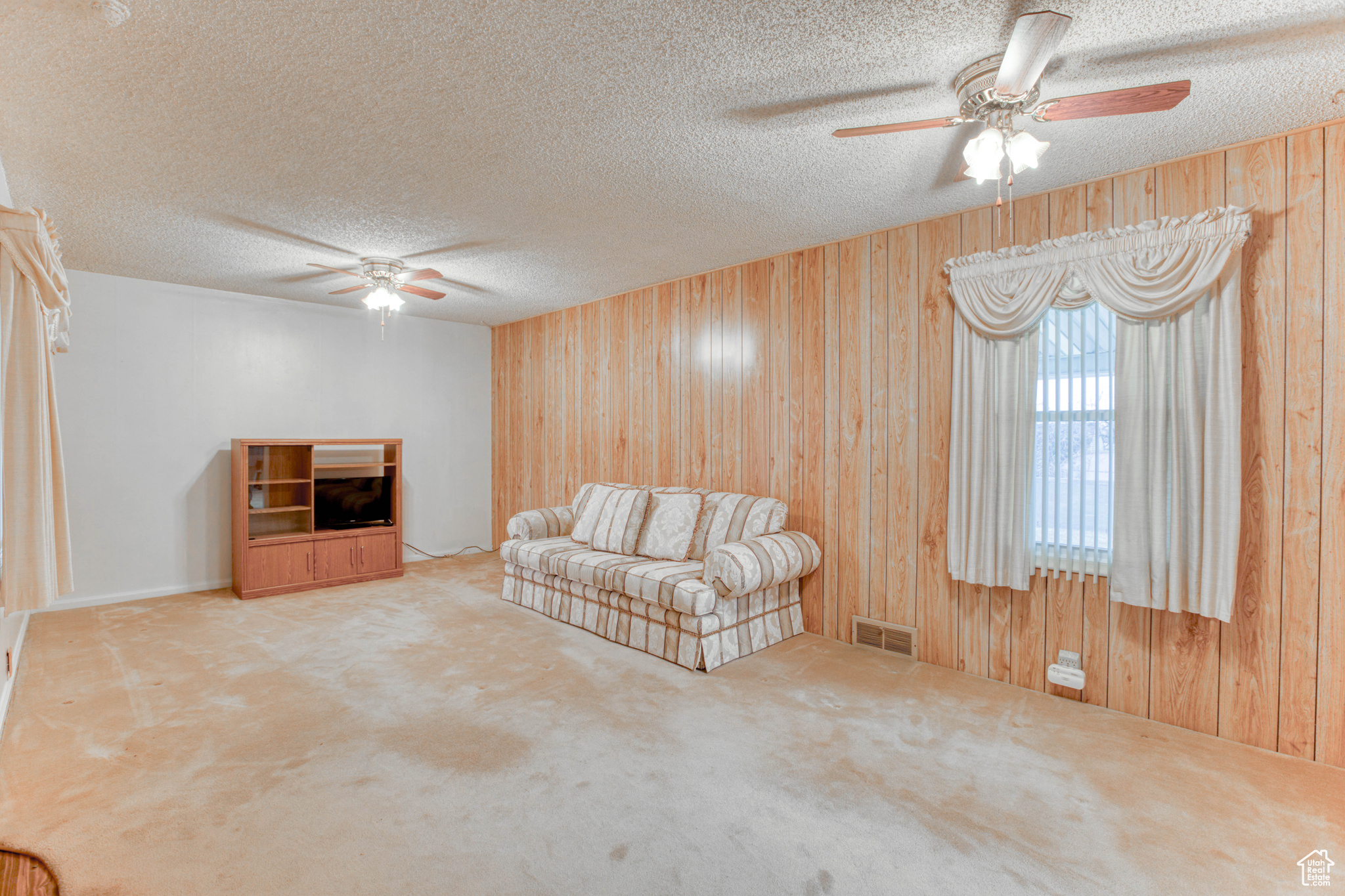 Unfurnished living room with ceiling fan, carpet floors, a textured ceiling, and wood walls