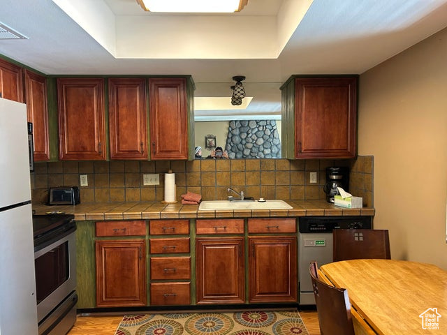 Kitchen featuring tile counter and backsplash, sink, stainless steel range with electric top, white fridge, and a dining table