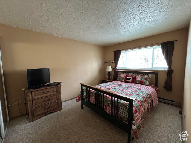 Bedroom with light colored carpet, a textured ceiling, and baseboard heating