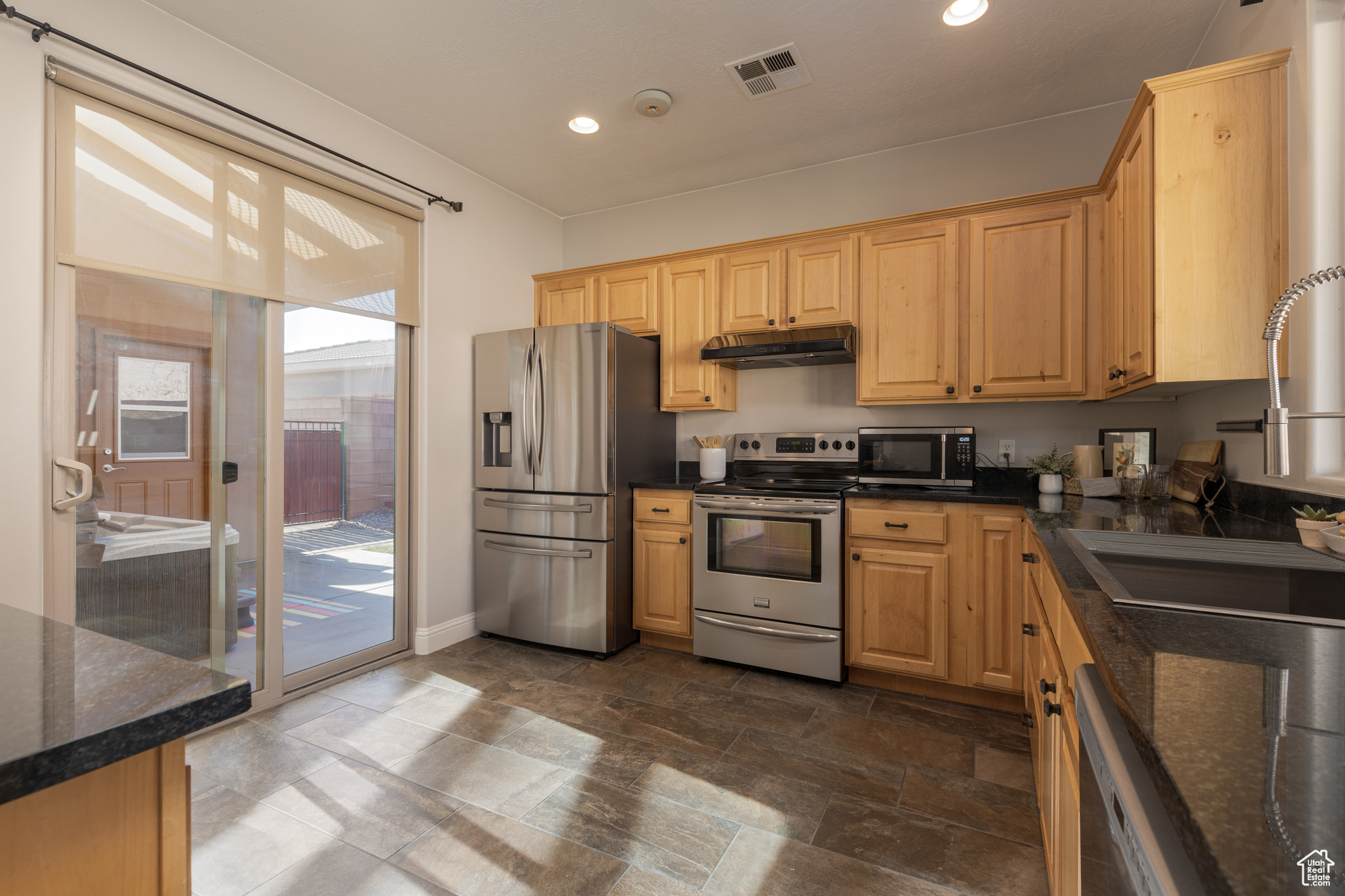 Kitchen featuring dark stone counters, recessed lighting, under cabinet range hood, and appliances with stainless steel finishes