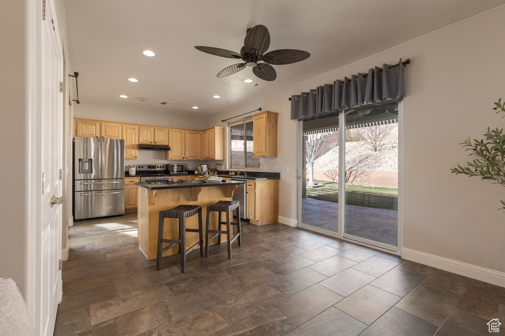 Kitchen with a kitchen bar, light brown cabinets, a kitchen island, dark countertops, and appliances with stainless steel finishes