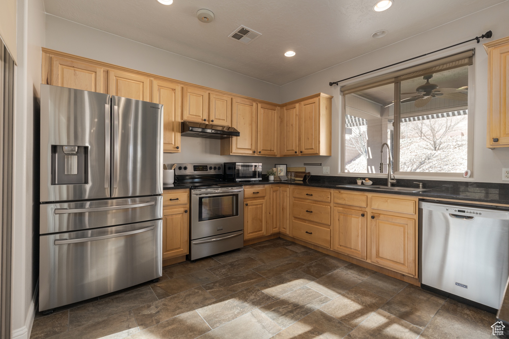 Kitchen featuring a sink, stainless steel appliances, under cabinet range hood, and dark countertops