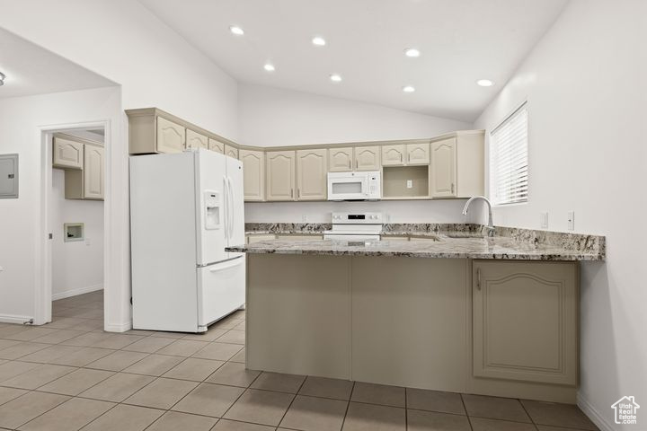 Kitchen featuring white appliances, light tile patterned floors, lofted ceiling, light stone countertops, and cream cabinets