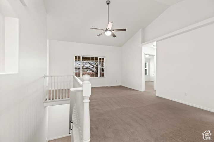 Carpeted spare room featuring vaulted ceiling and ceiling fan