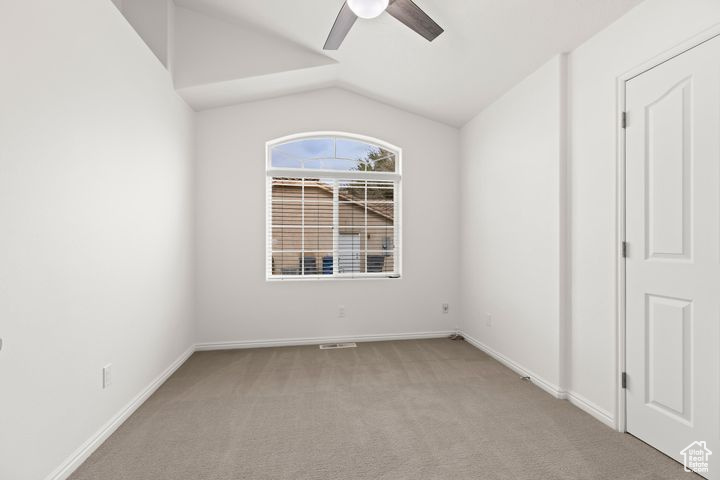 Empty room featuring light carpet, lofted ceiling, and ceiling fan