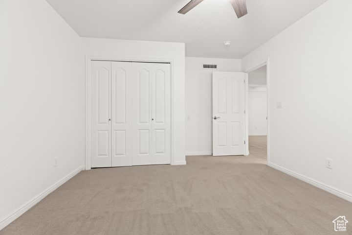Unfurnished bedroom featuring a closet, light colored carpet, and ceiling fan