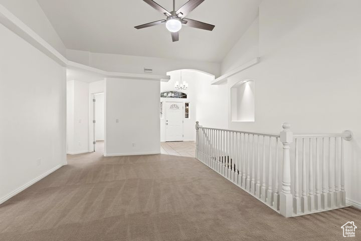 Carpeted spare room featuring ceiling fan with notable chandelier and high vaulted ceiling
