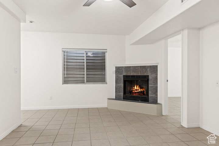 Unfurnished living room featuring a fireplace, ceiling fan, and light tile patterned floors