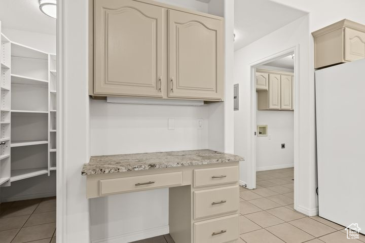 Kitchen featuring light tile patterned floors, cream cabinetry, built in desk, and white refrigerator