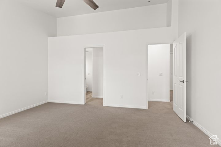 Unfurnished bedroom featuring ceiling fan, ensuite bath, and light colored carpet