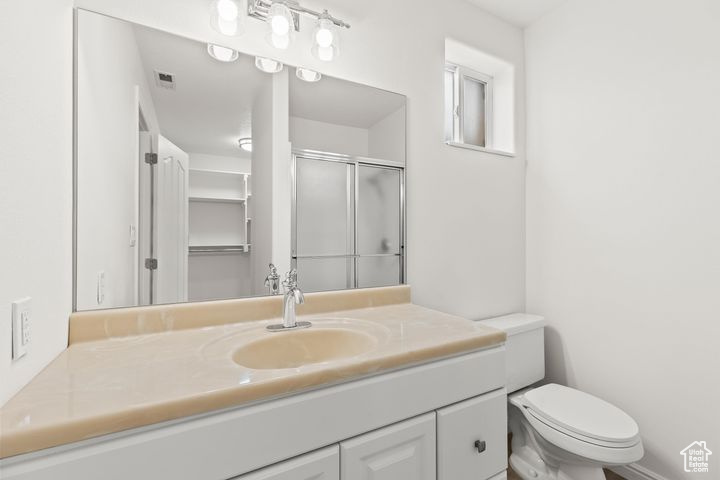 Bathroom featuring toilet, a shower with door, and vanity