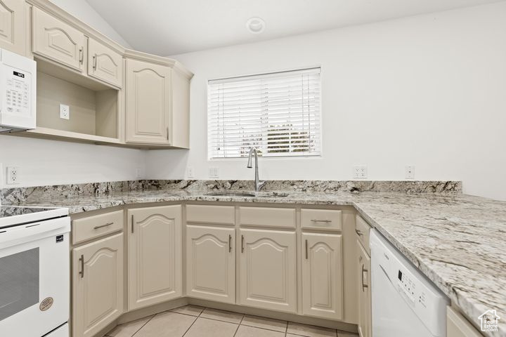 Kitchen featuring cream cabinetry, white appliances, light stone countertops, light tile patterned floors, and sink