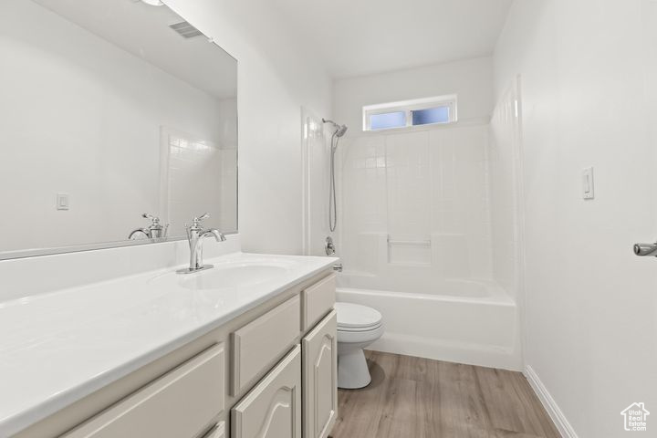 Full bathroom with hardwood / wood-style flooring, toilet, vanity, and washtub / shower combination