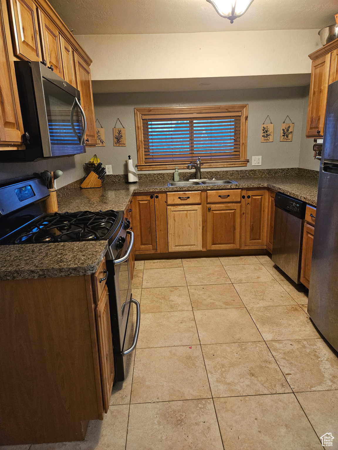 Kitchen with light tile patterned floors, appliances with stainless steel finishes, brown cabinets, and a sink
