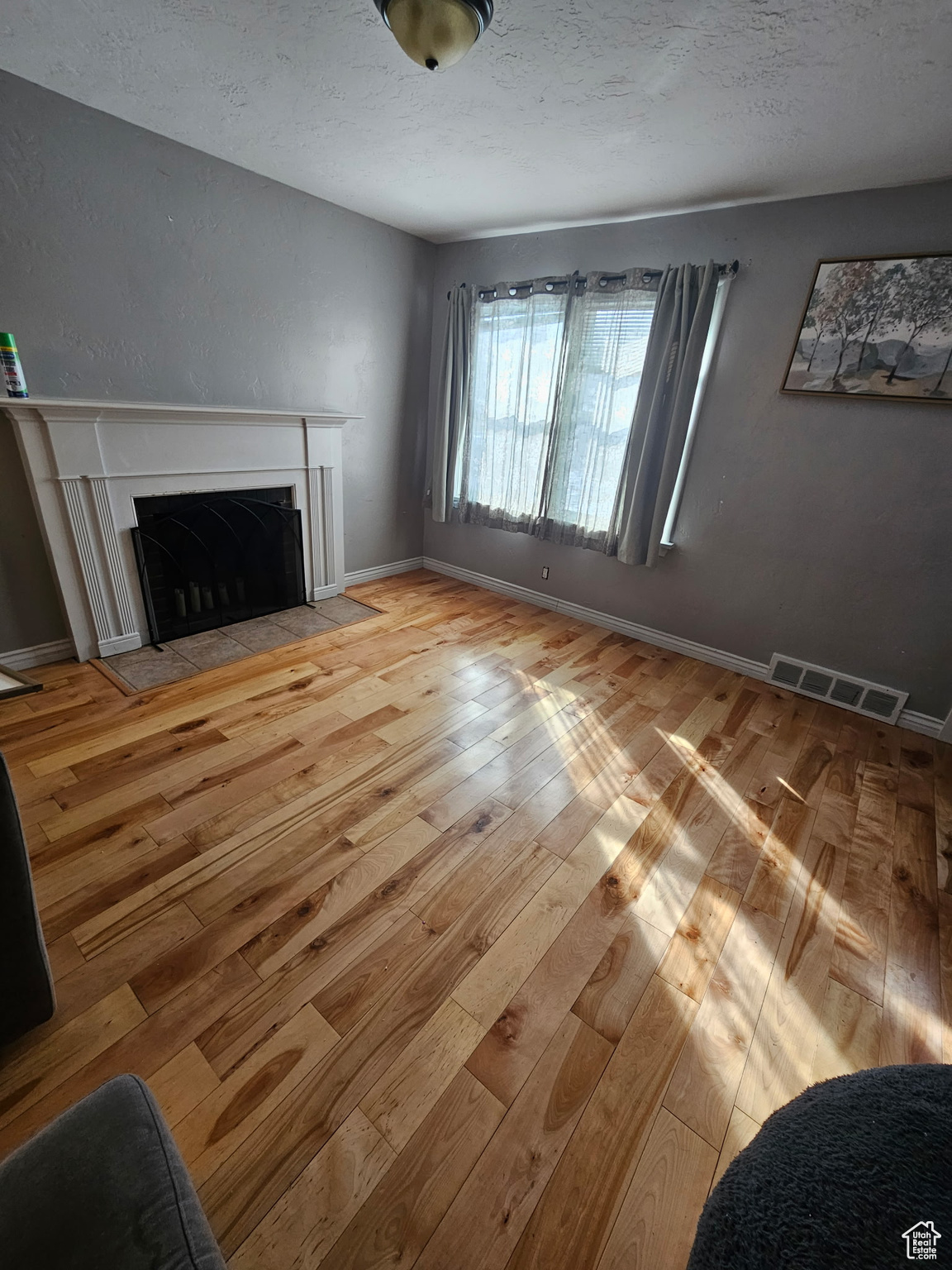 Unfurnished living room with a fireplace with flush hearth, visible vents, light wood-style flooring, and a textured ceiling
