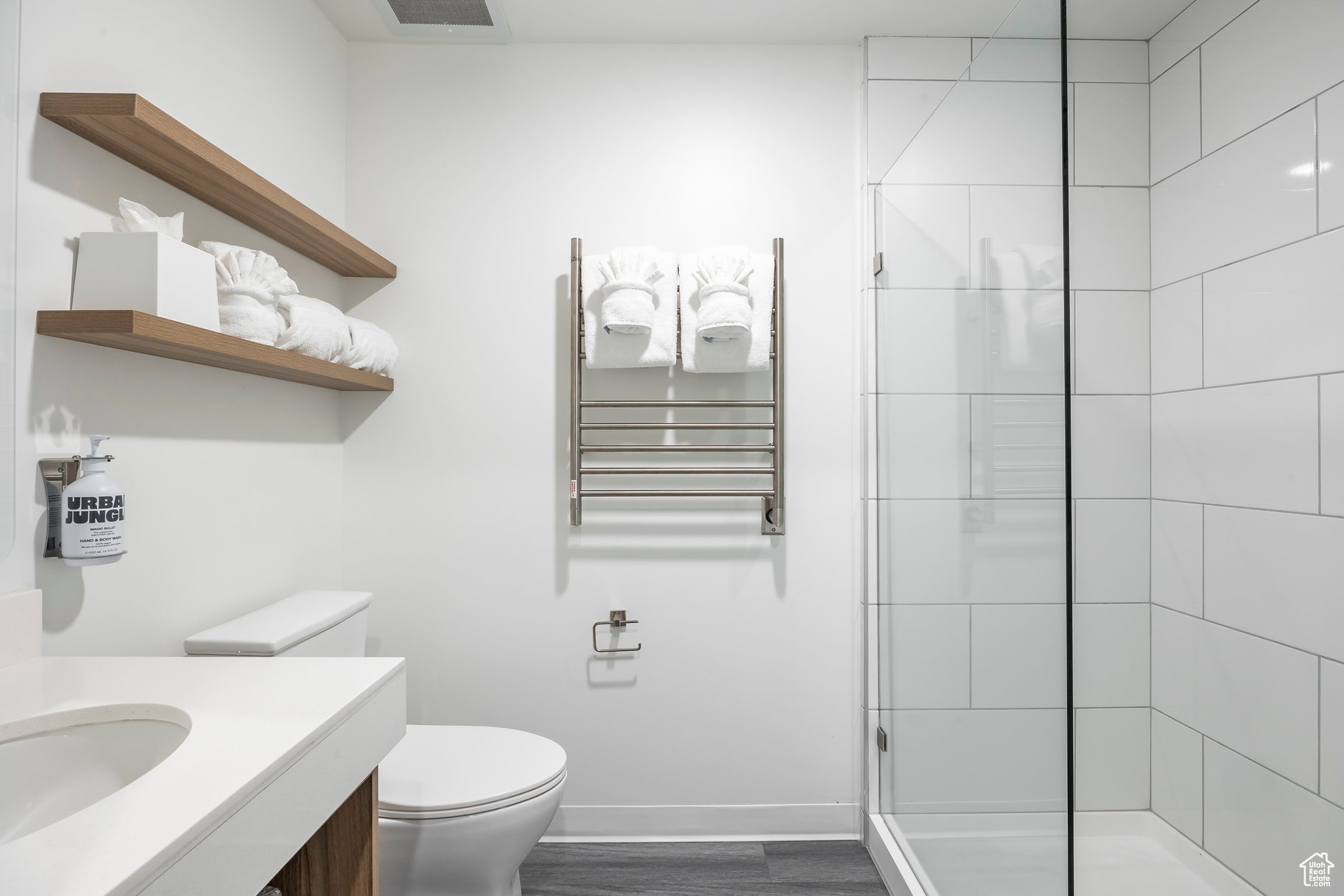 Bathroom with hardwood / wood-style floors, radiator heating unit, vanity, tiled shower, and toilet