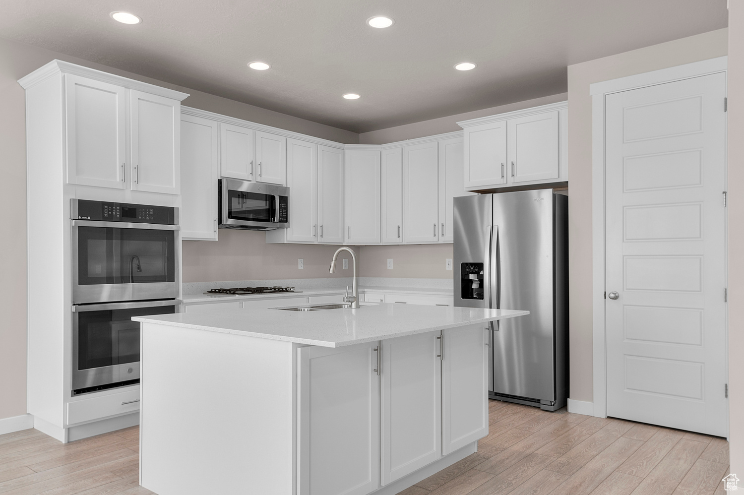 Kitchen with an island with sink, light wood-type flooring, stainless steel appliances, sink, and white cabinets