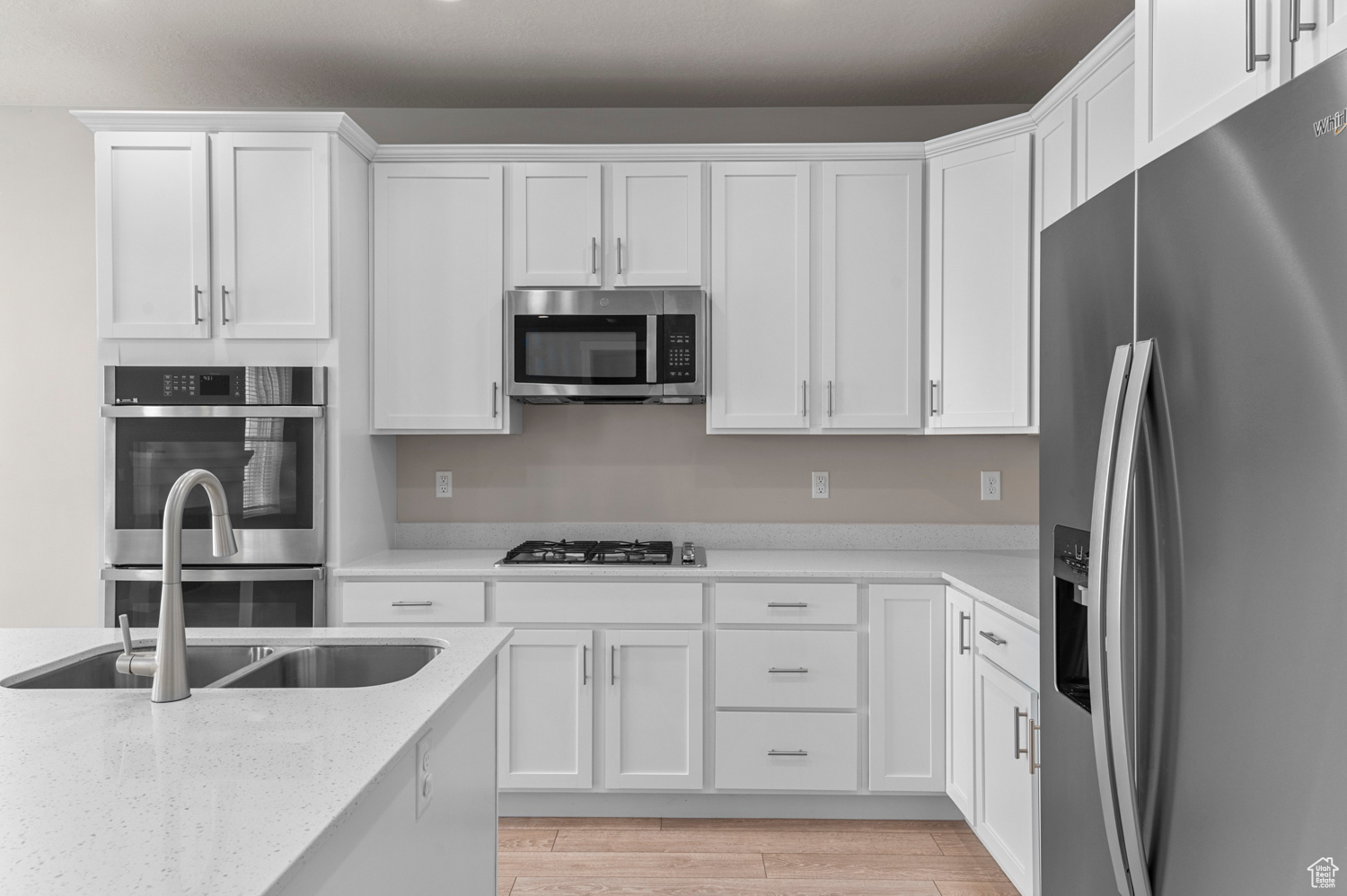 Kitchen featuring white cabinetry, stainless steel appliances, light stone countertops, light hardwood / wood-style floors, and sink