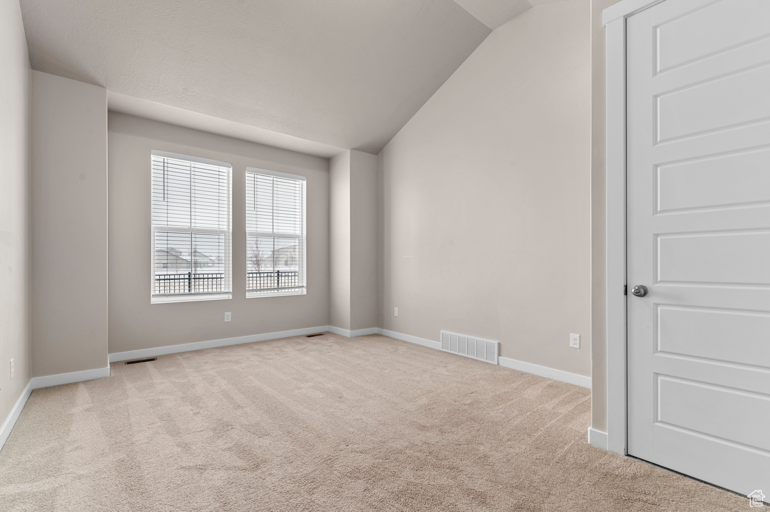 Empty room with light colored carpet and lofted ceiling