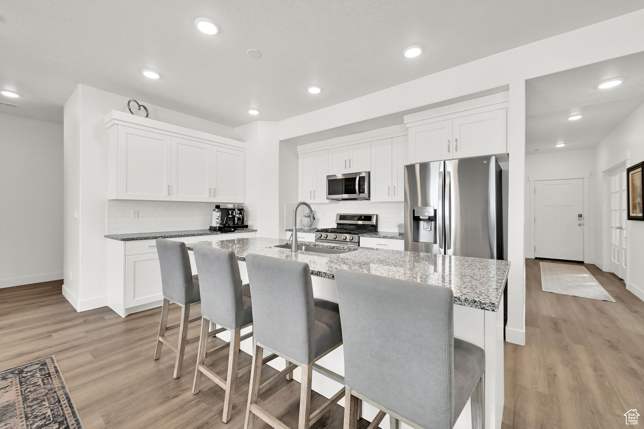 Kitchen with a kitchen island with sink, stainless steel appliances, light stone counters, white cabinets, and a kitchen bar
