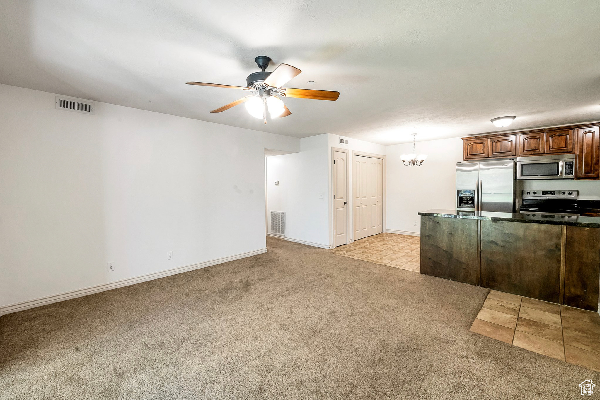 Kitchen with appliances with stainless steel finishes, hanging light fixtures, light colored carpet, and ceiling fan