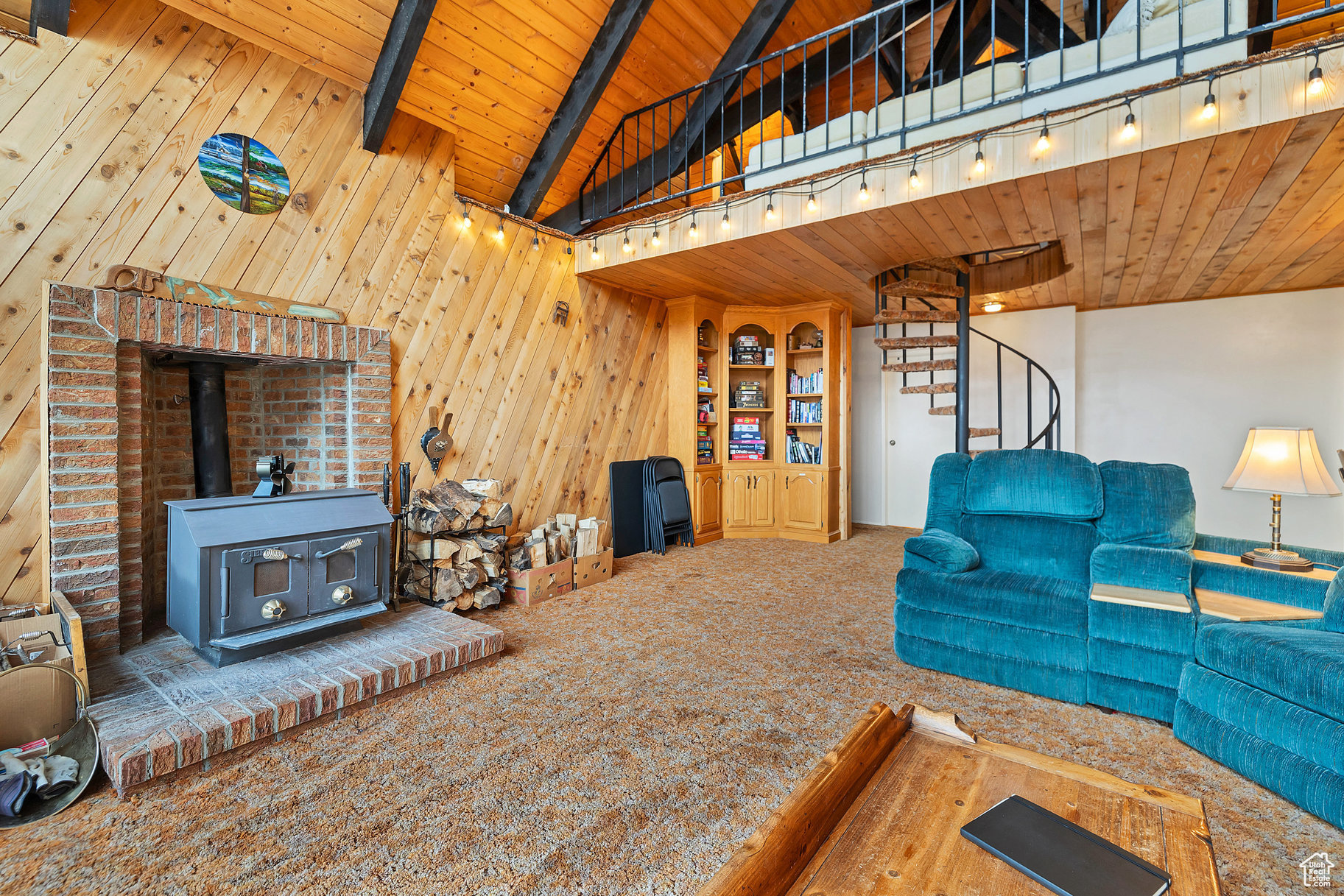 Carpeted living room with a wood stove, beam ceiling, wooden ceiling, wooden walls, and rail lighting