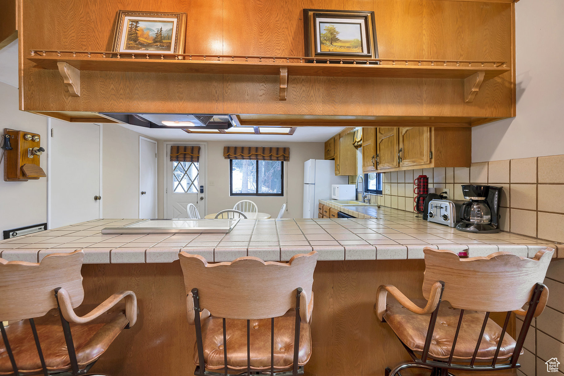 Kitchen featuring white fridge, sink, a kitchen breakfast bar, kitchen peninsula, and tile counters