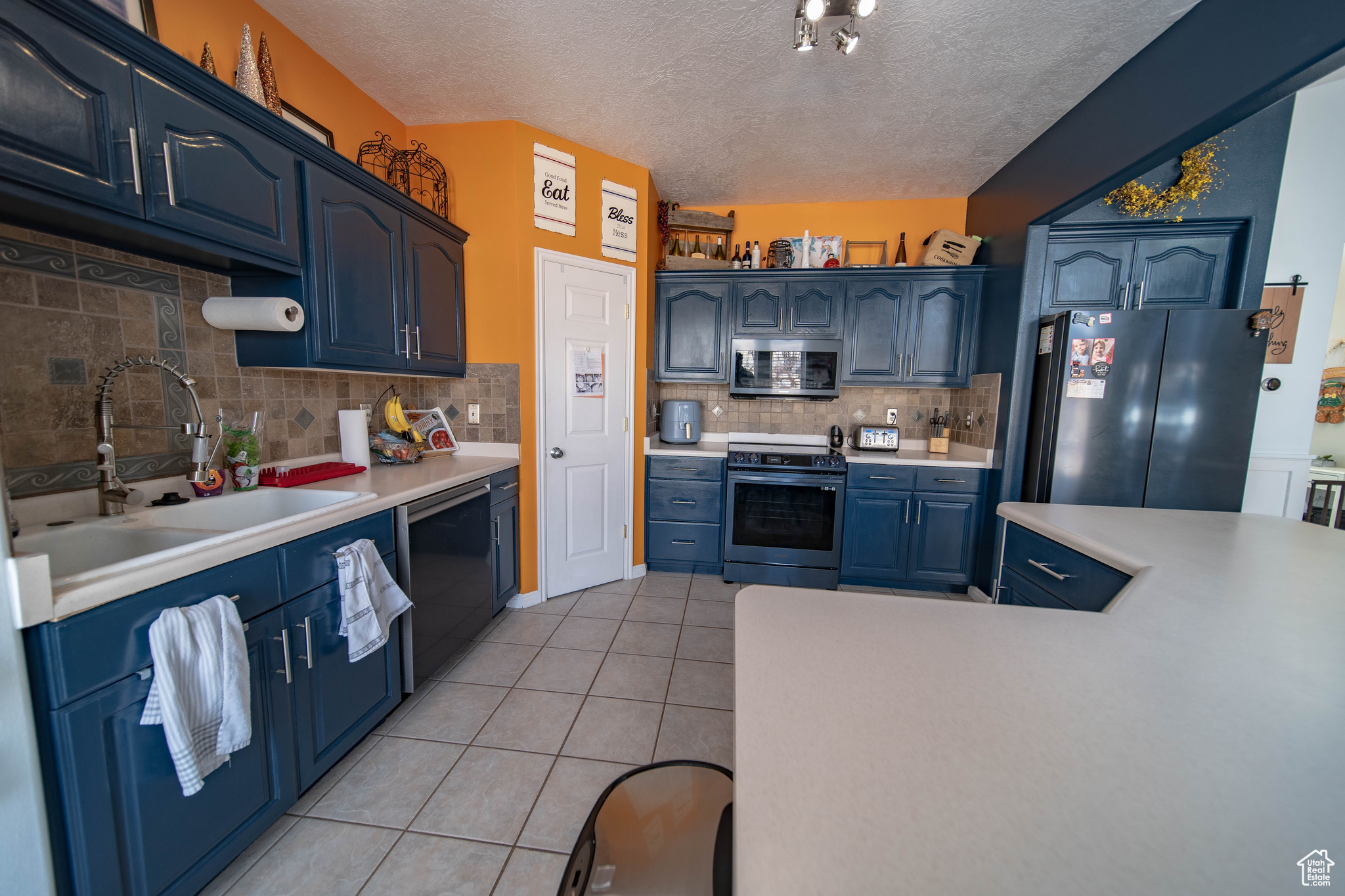 Kitchen featuring blue cabinetry, black appliances, decorative backsplash, light tile patterned floors, and sink