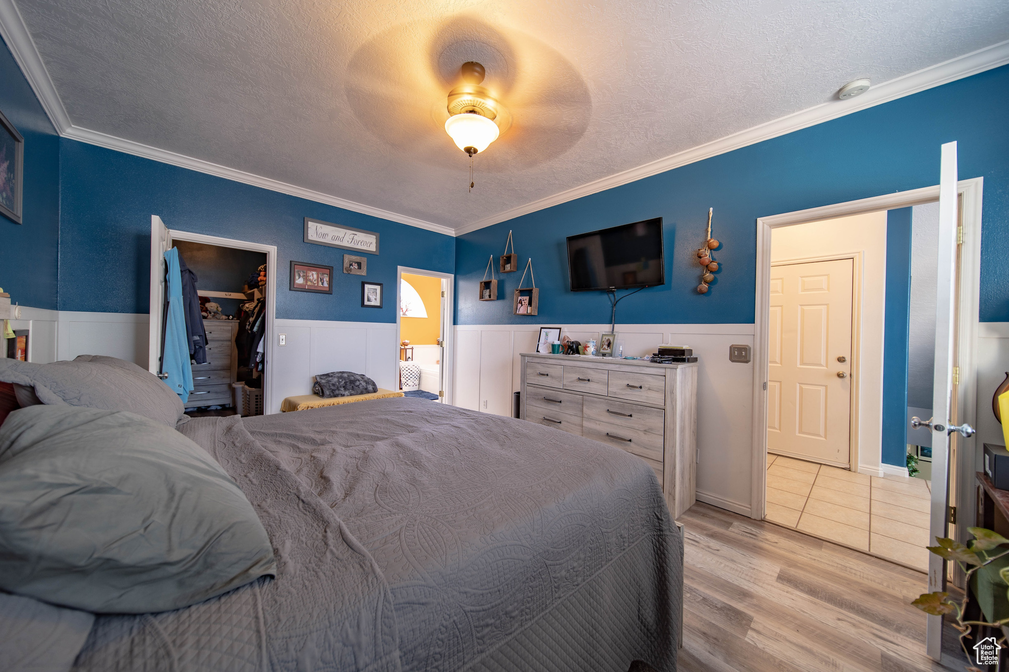 Bedroom with a textured ceiling, crown molding, a walk in closet, and light hardwood / wood-style flooring