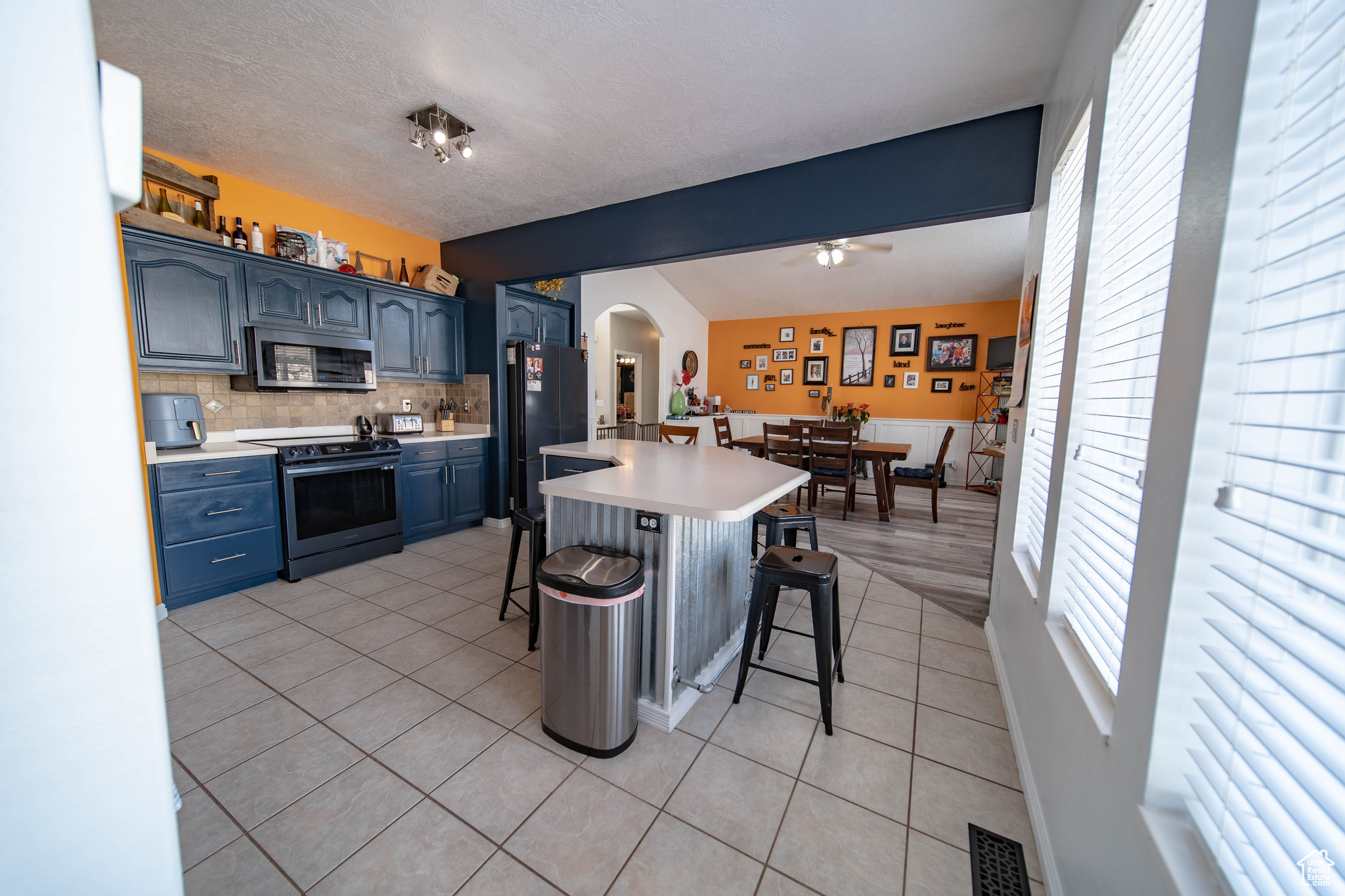 Kitchen with light tile patterned floors, a breakfast bar, backsplash, blue cabinets, and stainless steel appliances