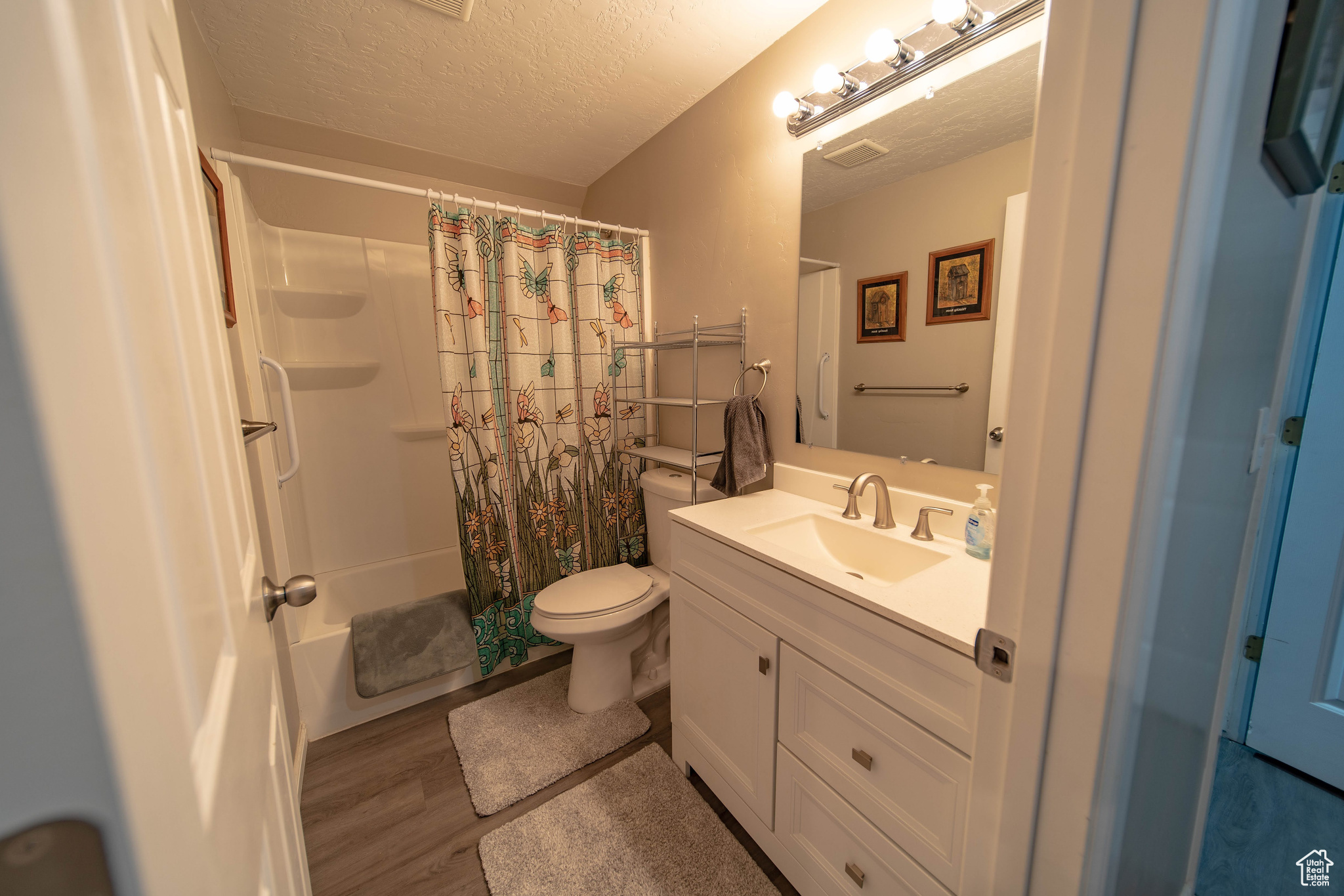 Full bathroom with toilet, wood-type flooring, a textured ceiling, shower / bath combo, and vanity