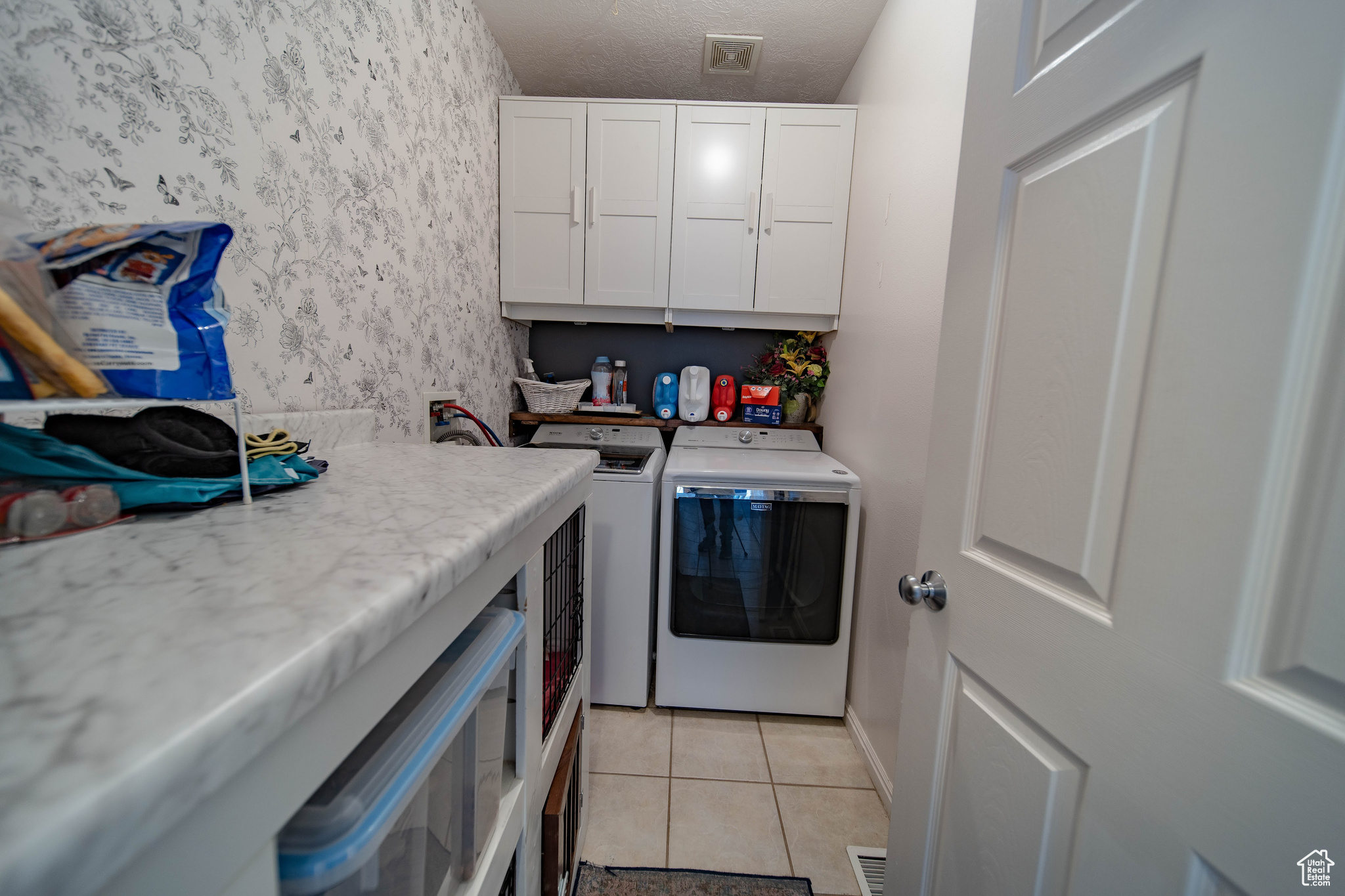 Laundry area featuring light tile patterned flooring, cabinets, washer and clothes dryer, and a textured ceiling