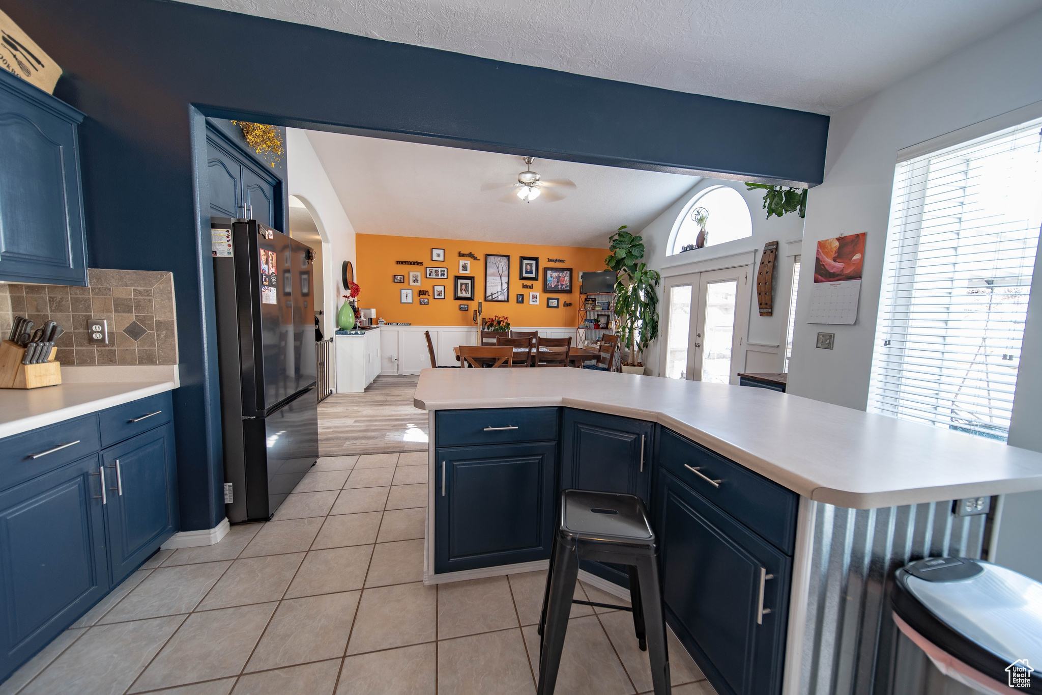 Kitchen with vaulted ceiling with beams, backsplash, plenty of natural light, blue cabinets, and black fridge