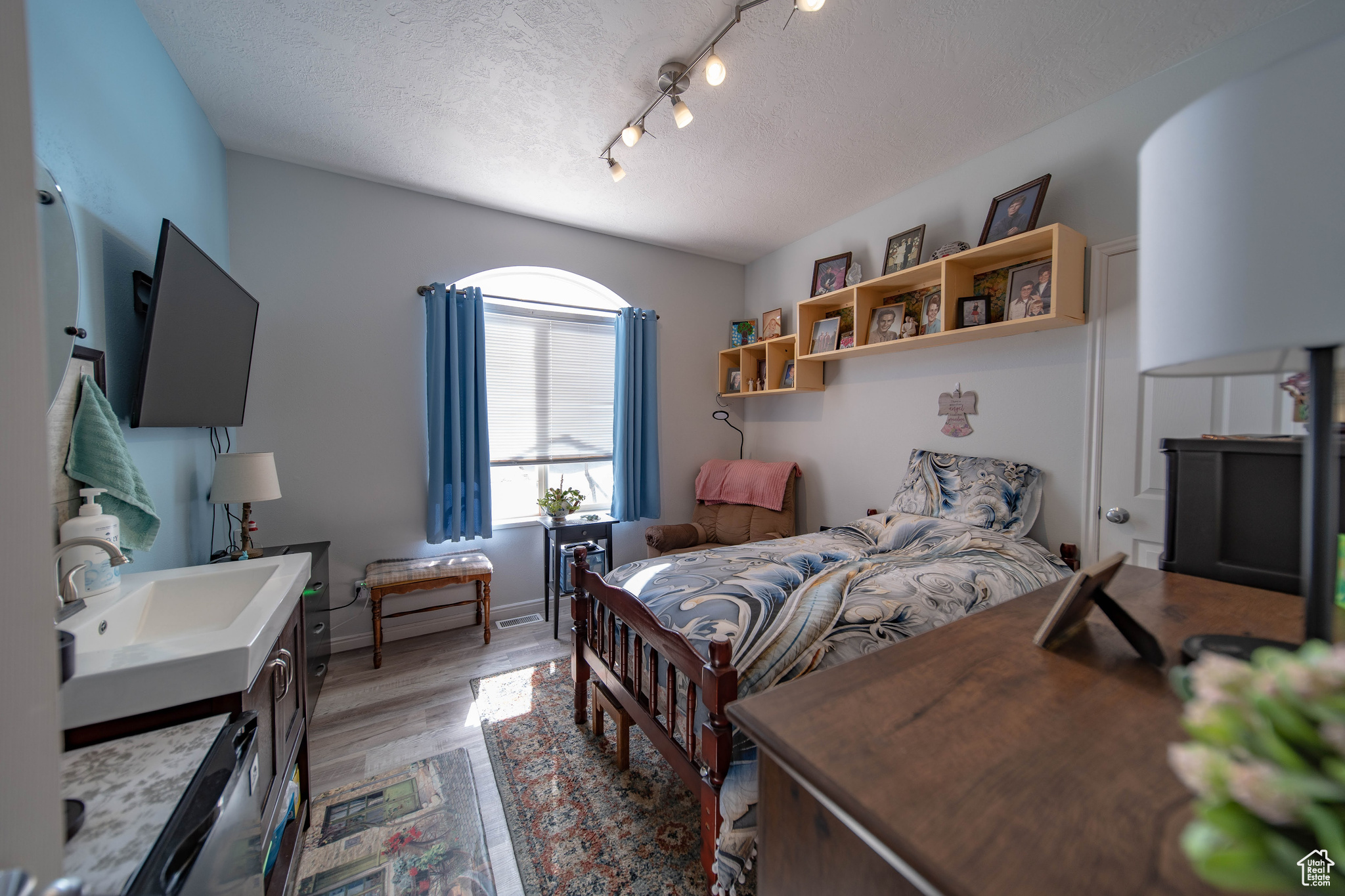 Bedroom with track lighting, light hardwood / wood-style flooring, sink, and a textured ceiling