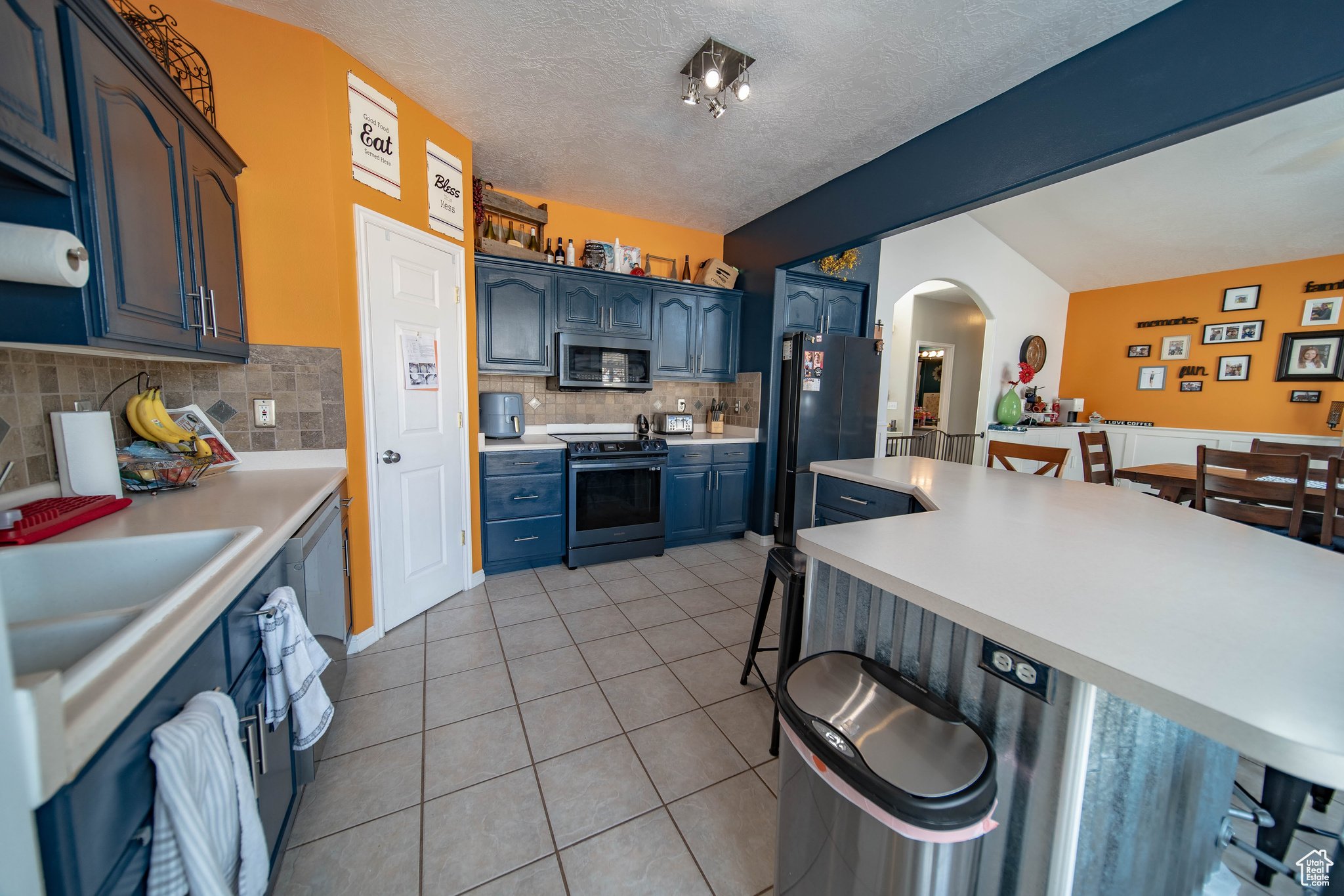 Kitchen with tasteful backsplash, blue cabinetry, stainless steel appliances, light tile patterned floors, and a kitchen bar
