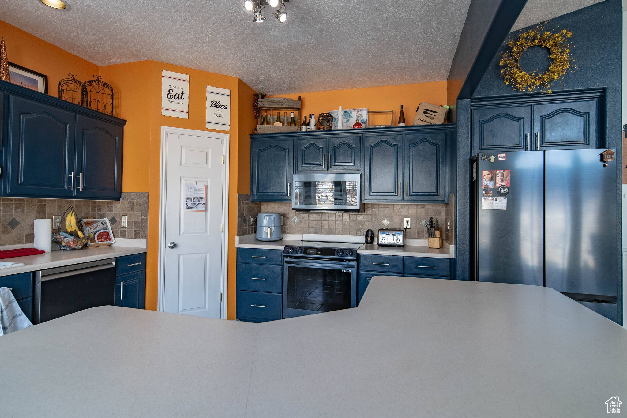 Kitchen featuring decorative backsplash, blue cabinets, stainless steel appliances, and a textured ceiling